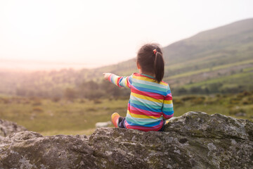 Naklejka premium young girl sitting on the rock and pointing into the distance on the Mourne Mountain ,Northern Ireland