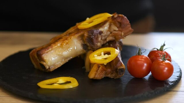 A chef in black gloves serves pepper ribs on a black slate serving Board. close up.