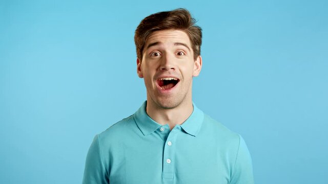 Amazed european man shocked, saying WOW. Handsome guy surprised to camera over blue background.