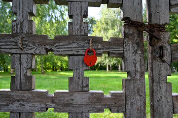 A large red padlock hanging on an old carved wooden gate.