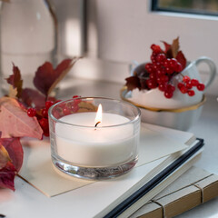 iron cup of coffee with a spoon on the windowsill among a vase with branches and viburnum berries, a sweater, an open book and a candle. Photo for Instagram