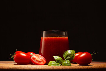 Fresh tomato juice in a glass with fresh basil leaves and tomatoes on wooden table.Close up of healthy drink.