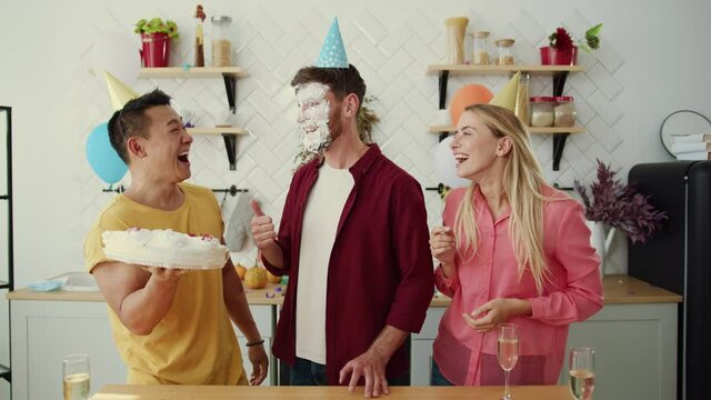 Funny excited three friends smashing their faces into birthday cake celebrating anniversary party at home. Fun and entertainment. Humor concept.