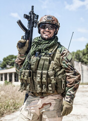 Fototapeta premium Army soldier, special forces infantryman, Navy SEALs fighter in camouflage uniform, combat helmet and plate carrier, armed submachine gun. Half-length portrait of happy smiling commando shooter