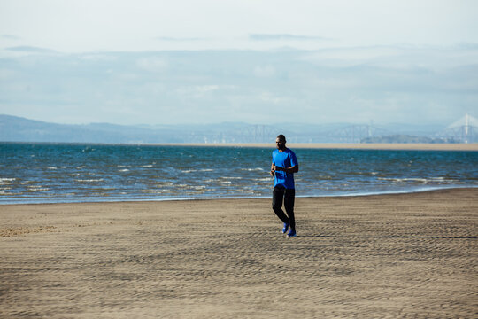 A man running alongside the sea, Edinburgh rail bridge is in the distance