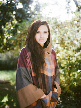 Beautiful woman wearing hooded cloak and standing in autumnal garden