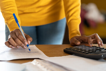Close up of Black woman using calculator, holding pen, writing make note with calculate. Female in...