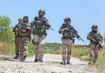 Army soldiers team in combat uniform, load carriers and helmets running on countryside road, aiming...