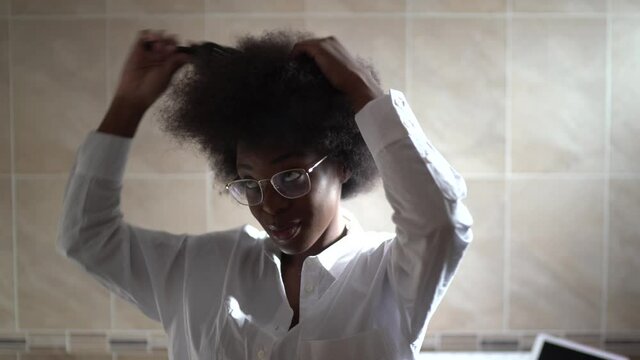 African American woman with lots of hair combing her hair in front of a mirror.