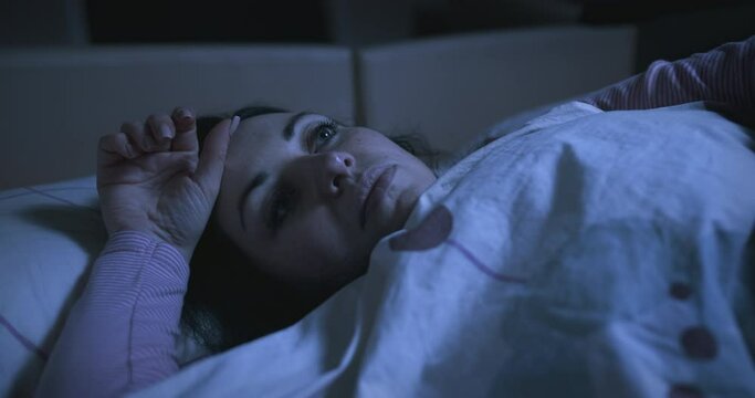 Sad pensive woman with an apathetic look lying on the bed and looking at the ceiling. Sleep problems, insomnia, thinking about her problems, can not sleep. Restless thoughts at night. 