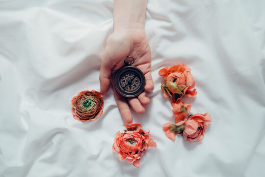 hand holding a compass over white sheets surrounded by orange flowers