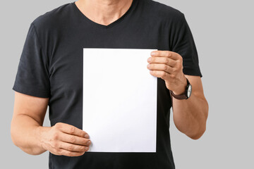 Man with blank paper sheet on grey background