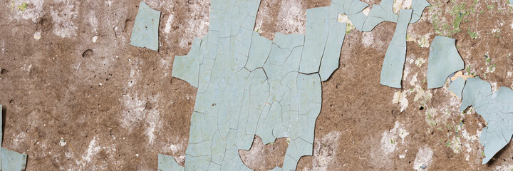 Peeling paint on the wall. Panorama of a concrete wall with old cracked flaking paint. Weathered rough painted surface with patterns of cracks and peeling. Wide panoramic texture for design background