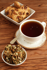 Oatmeal cookies with walnuts and raisins, sugar-coated pumpkin seeds cookies in a bowls and a cup of black tea on a wooden table. Closeup
