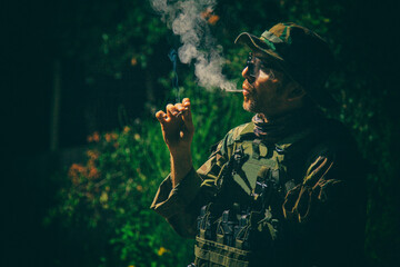 Commando soldier in camouflage uniform, ballistic glasses and bonnie, inhale cigarette smoke,...
