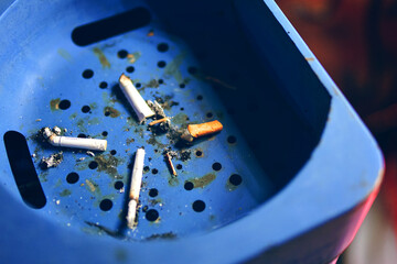 Large ashtray with cigarette butts. Blue trash can with ashtray. Used cigarettes. Waste.