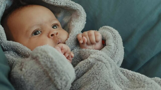 Macro of cute mixed-race baby girl wearing grey warm rompers lying in bed at home
