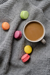Background with gray plaid, coffee, cappuccino and multicolored appetizing macaroons, top view, flat lay. home comfort, warmth, care, tenderness.