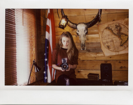 instant film photo of yang women with camera in the wooden cabin with vintage map and skull on the wall