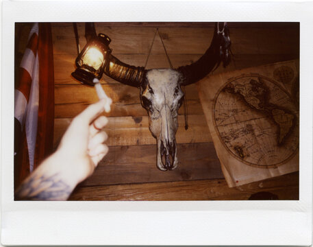 instant film photo of the hand with cigarette and wall with vintage map and buffalo skull