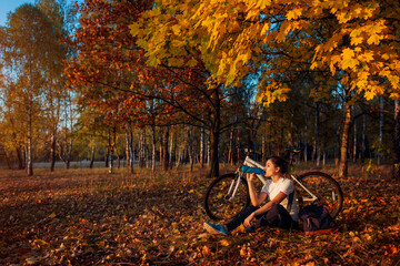 Young woman drinks water after workout on bike. Healthy lifestyle. Riding bicycle in autumn forest.