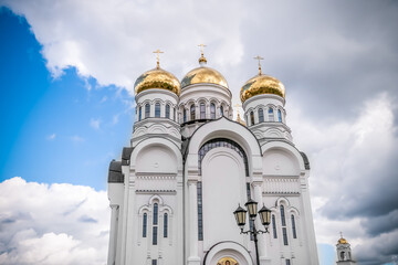 Golden domes, cupolas with Eastern Orthodox crosses on a white Church against a blue sky with clouds