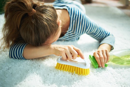 tired woman with cleaning agent and brush laying on carpet