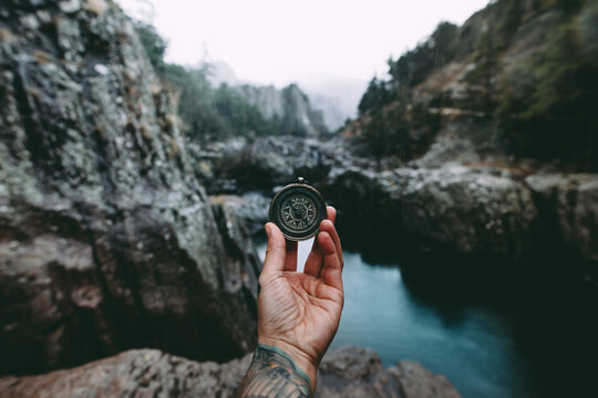 tattoed hand holding a compas behind a beautiful valley view