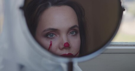 Beautiful young woman applying makeup clown on the face at home