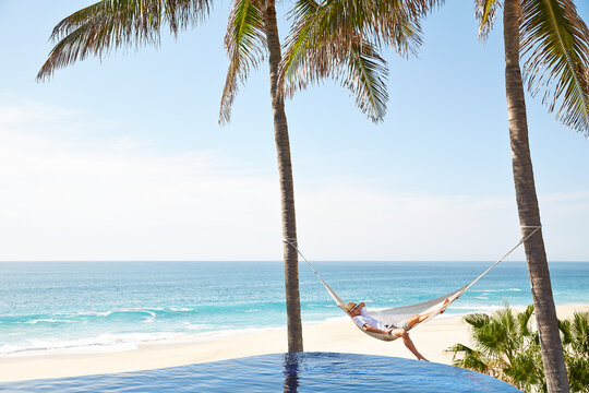 Man relaxing in hammock beside pool at tropical beach location
