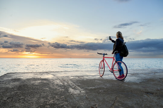 Woman with bike taking photo of sunrise on pier.