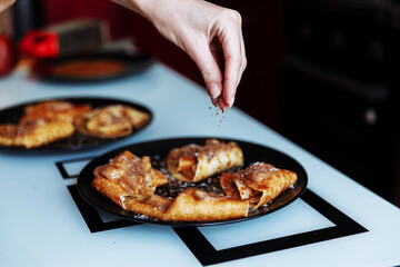 Woman's hand decorates pancakes with a chocolate, fruits kiwi and banana. Black plate, white table
