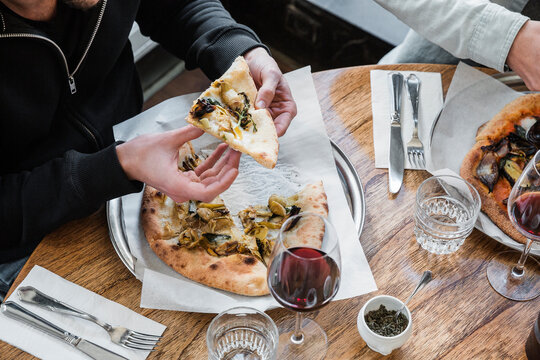 Anonymous man eating a slice of pizza with friends in restaurant