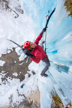 Female alpinist ice climbing a frozen waterfall