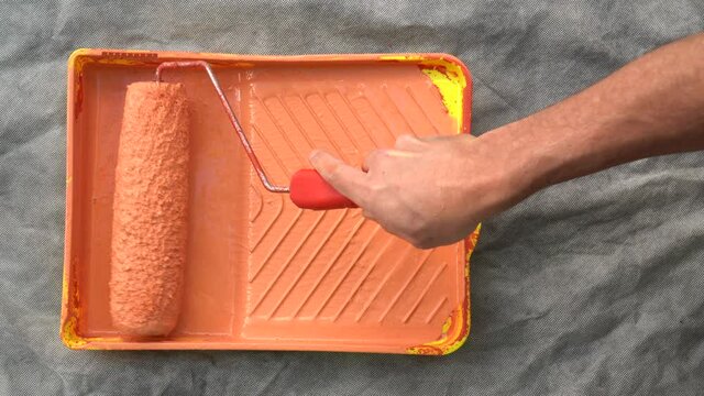 Close up of man hand preparing orange paint on tray with roller. Concept of DIY, paint, home, renovation, work, decoration, idea, home and hobby.