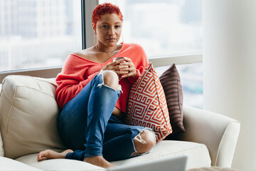 Black woman relaxing and drinking tea at home on couch