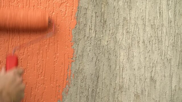 Close up of man hand painting old wall of apartment with roller and beautiful orange paint. Concept of DIY, paint, home, renovation, work, decoration, idea, home and hobby.