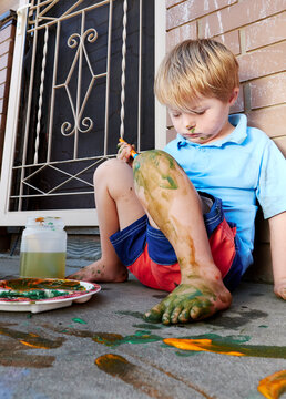 Boy Painting Self with Body Paint while Seated on Ground