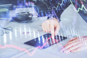 Double exposure of man's hands holding and using a digital device and forex graph drawing. Financial market concept.