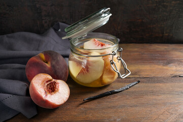 Peaches, fresh and preserved in a glass jar with vanilla to have canned fruits in winter, blue napkin and dark rustic wood, copy space, selected focus