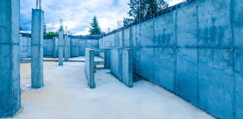 Erection buildings. Construction site. There is no one inside building under construction. Erection home made of concrete. Fir trees and sky in background. Concept - construction services.