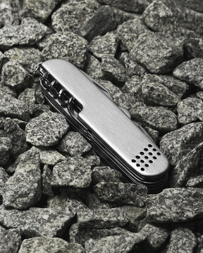 navaja suiza metalica  puesta sobre un fondo de piedras peque&ntilde;as grises con na luz suave