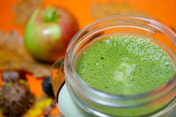Matcha latte in a clear glass on an autumn background with apples and leaves.