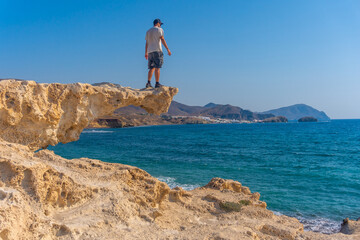 A young man perched on the rocks looking at Playa los Escullos in the natural park of Cabo de Gata, Nijar, Andalucia. Spain, Mediterranean Sea
