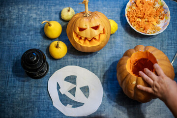 Woman carving big orange pumpkin into jack-o-lantern for Halloween holiday decoration.