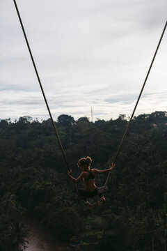 Brave young girl on hgh swing over tropical valley