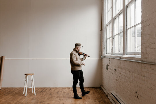 stylish young man standing and playing the violin in a studio