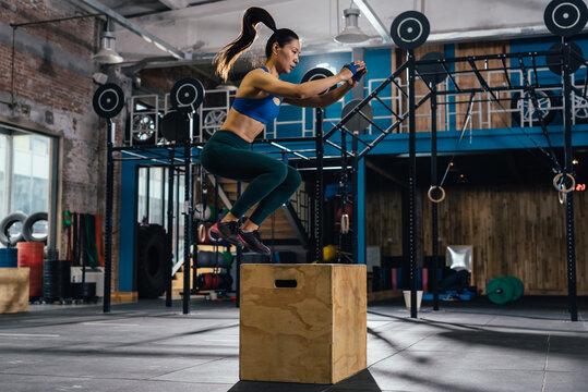 Young woman jumping mid air on gym box with arms reaching out