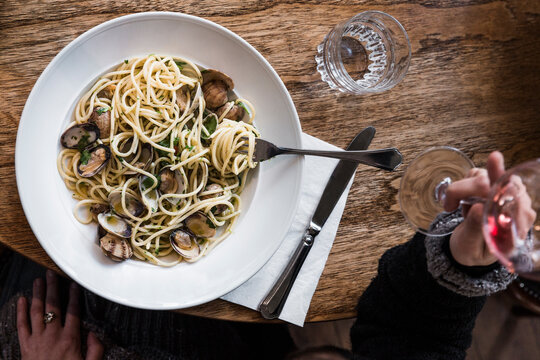 Woman drinking red wine while eating pasta with clams