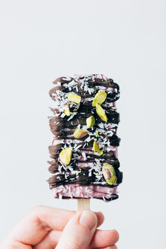 Woman holding up a cherry popsicle with coconut and pistachio nu